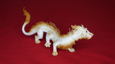 A long white dragon with six legs and a lion tail. Also a dog-like head, blue eyes and a friendly smile is presented on a red background.
