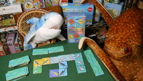 A plush shark and a large plush octopus are seated  at a table on which are dominoes with pictures of varous sharks.